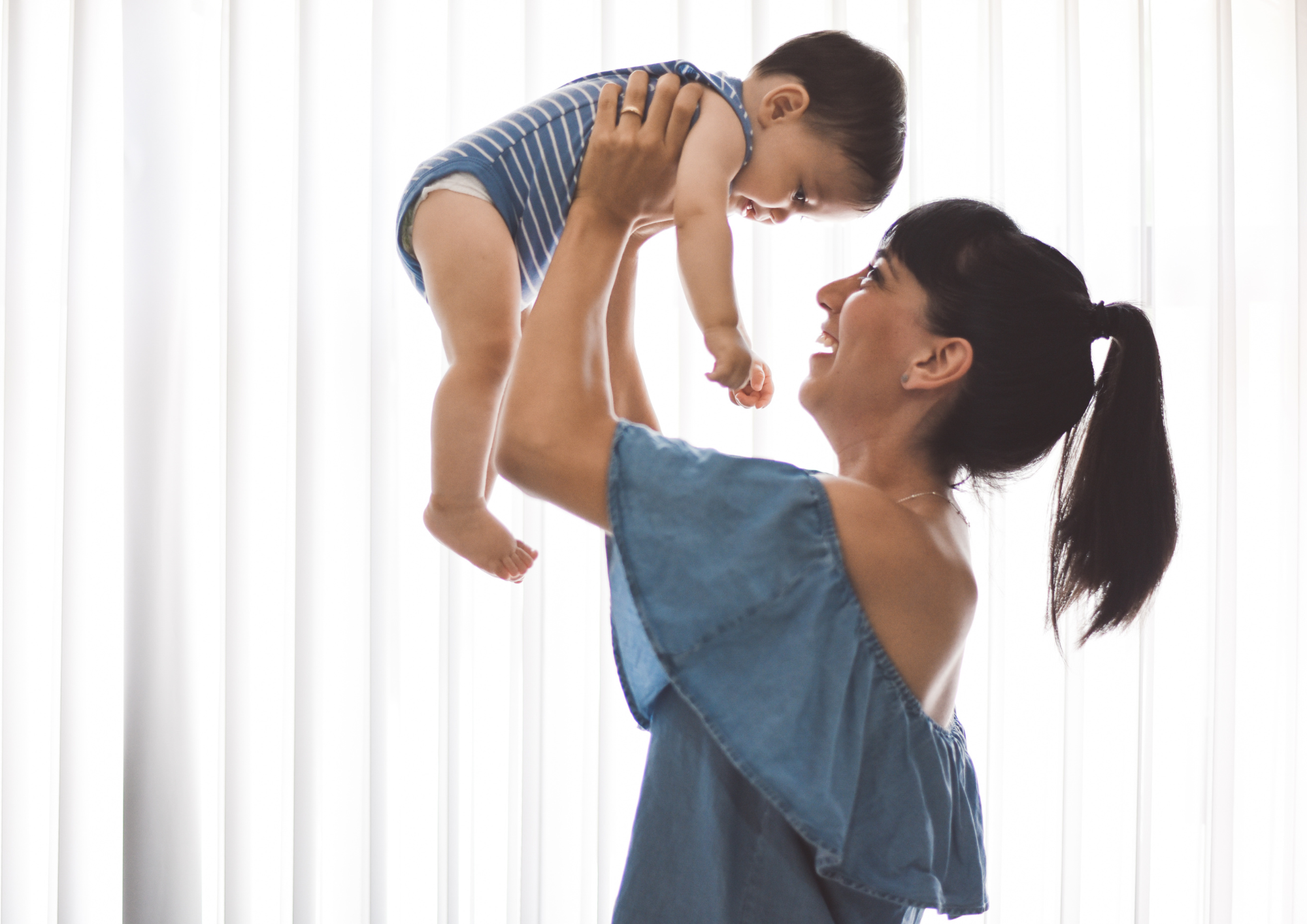 Mother lifting her smiling baby up into the light by the window
