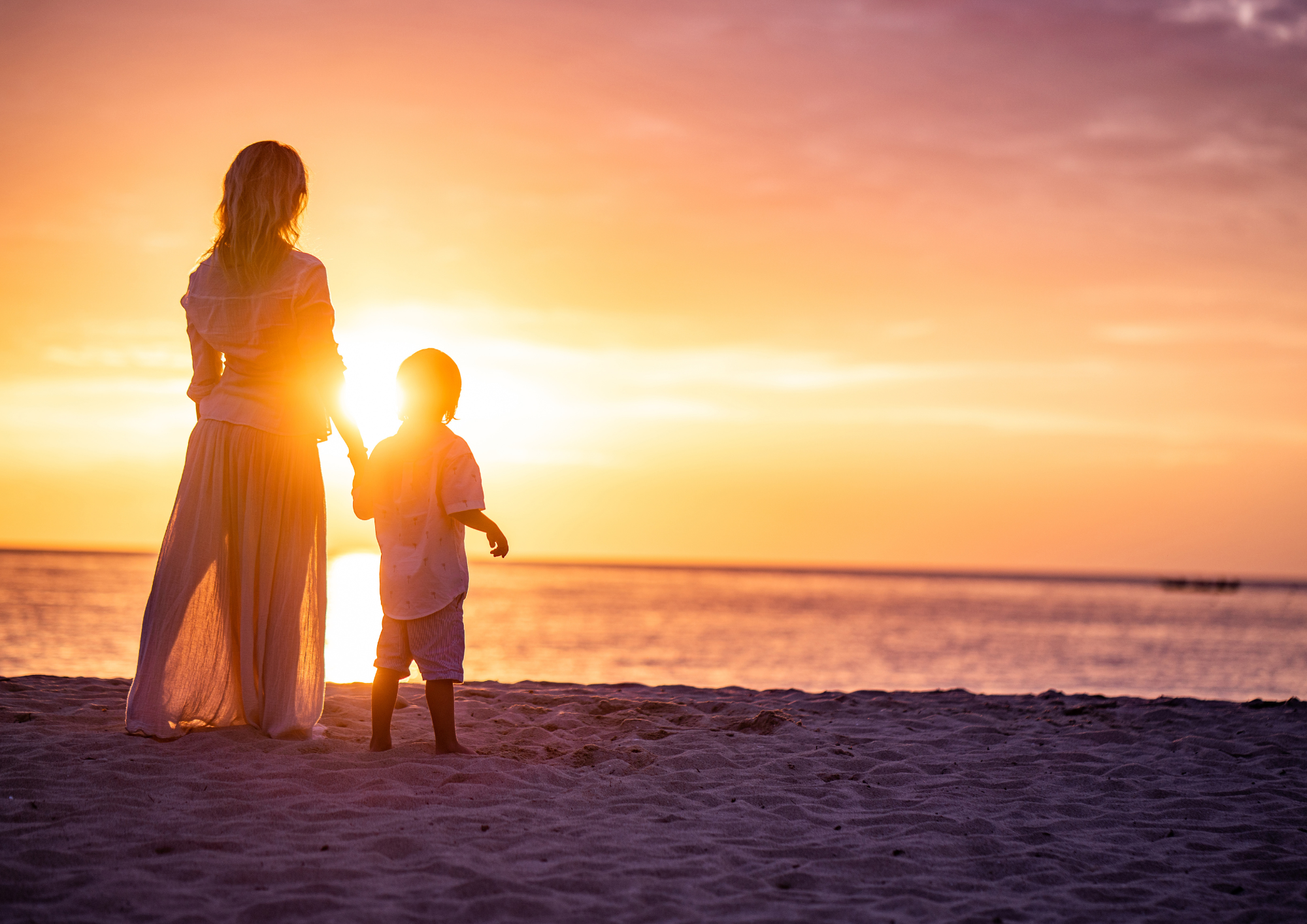 Mother and child holding hands on the beach at sunset