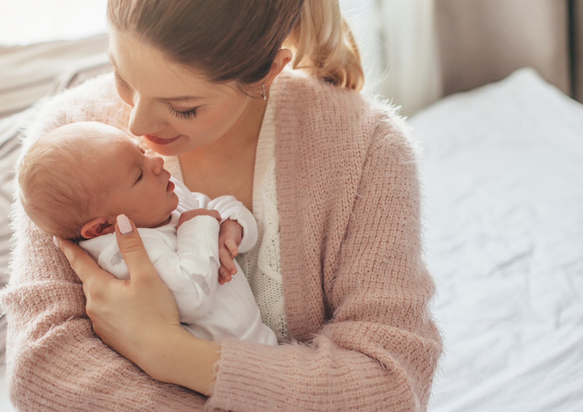 Mother nose to nose with her newborn, eyes closed, on the bed