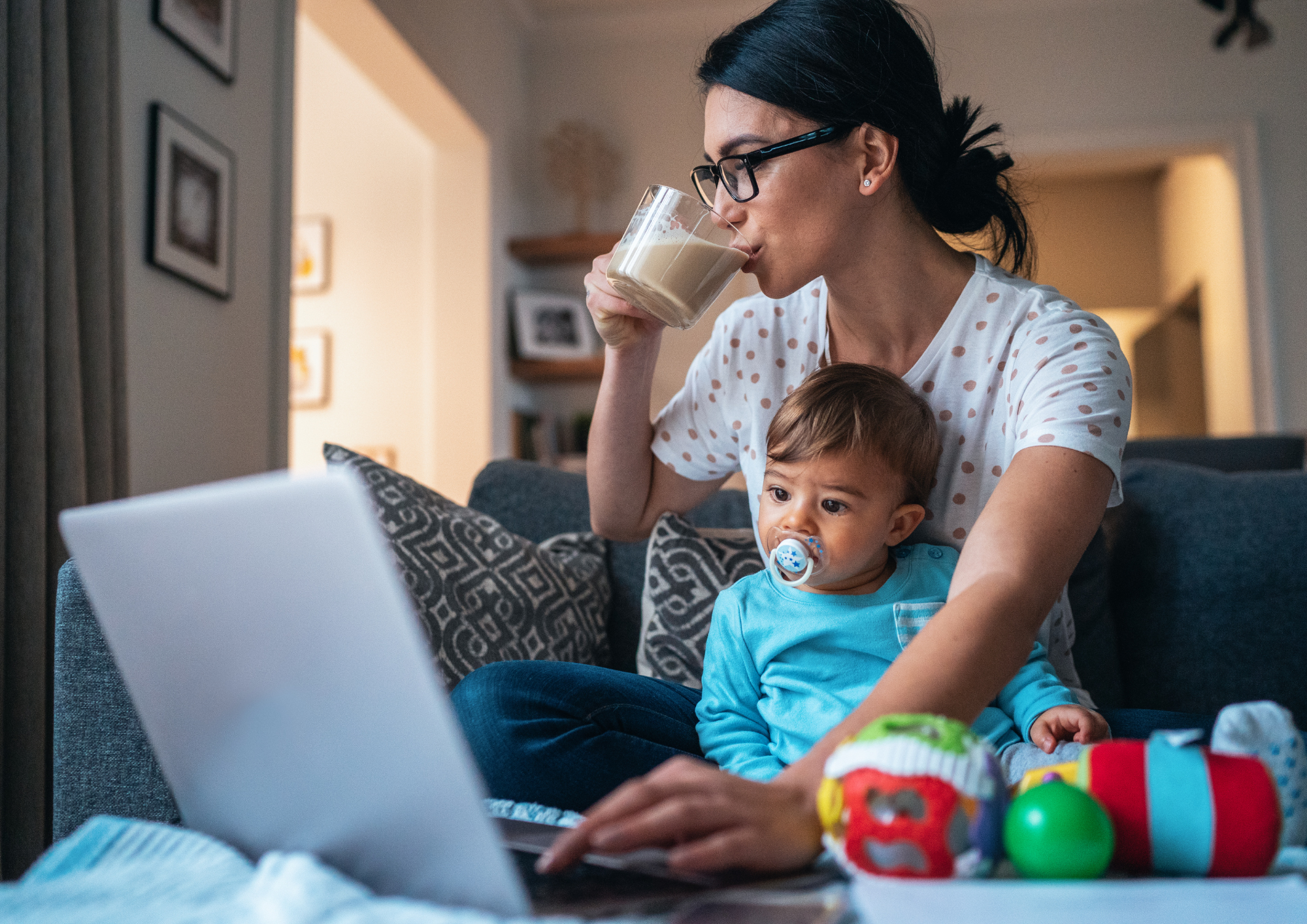 A tired mother on the sofa at night, baby in her lap, scrolling her phone for answers